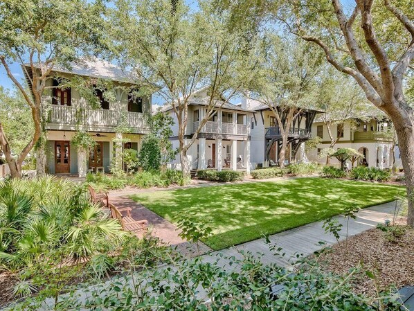 A two-story house with a front porch, surrounded by lush greenery and trees.