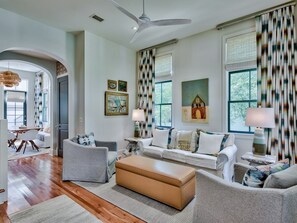 A spacious living room with a modern design, featuring a large sofa set, a coffee table, and a dining area in the background.