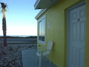 A yellow building with a white door marked '14', a white chair outside, and a palm tree. - Flagler Beach Motel and Vacation Rentals (Flagler Beach)