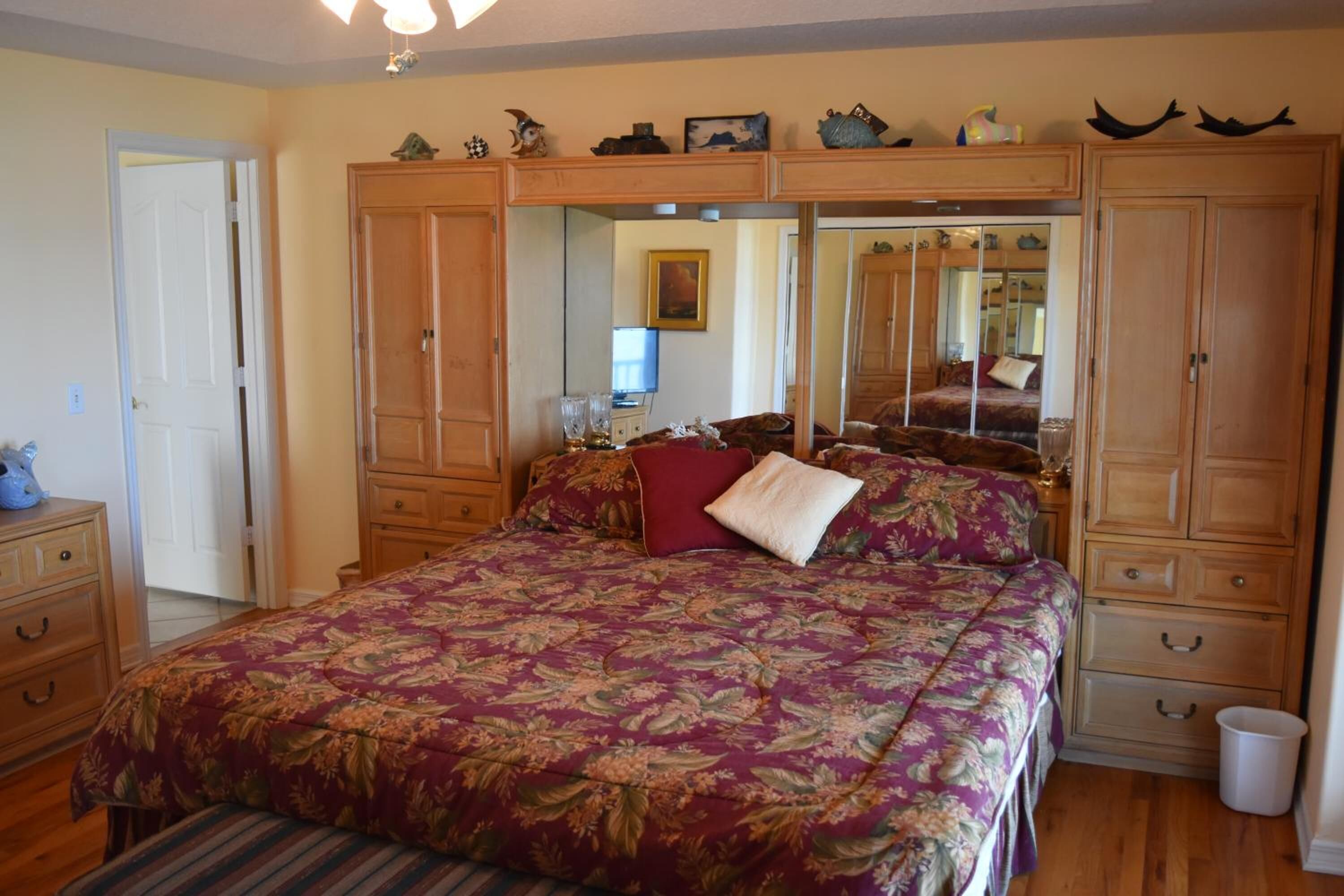 A bedroom with a large bed, wooden wardrobe, and a mirror cabinet.