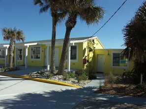 A yellow building with multiple doors and windows, surrounded by palm trees and a paved area. - Flagler Beach Motel and Vacation Rentals (Flagler Beach)