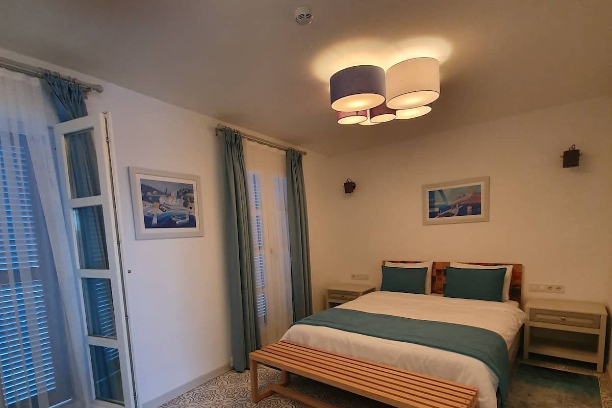 Ein Schlafzimmer mit einem Bett, Nachttischen, einer Bank, gemusterten Teppichen und Deckenleuchten.