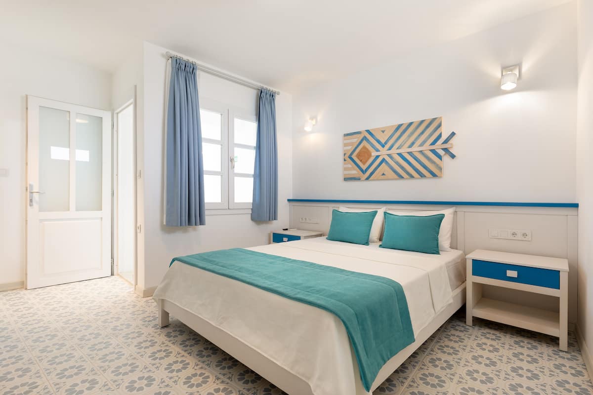 Ein Schlafzimmer mit einem Bett, Nachttischen, einem Wandbild und einem gemusterten Boden.