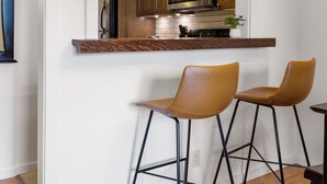 Una cocina moderna con armarios de madera, un microondas de acero inoxidable y una zona de bar con dos taburetes.