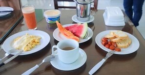 A breakfast table with plates of scrambled eggs, toast with sausage, a slice of watermelon, a cup of coffee, and a glass of orange juice. - Pousada Concha Dourada (Maragogi)