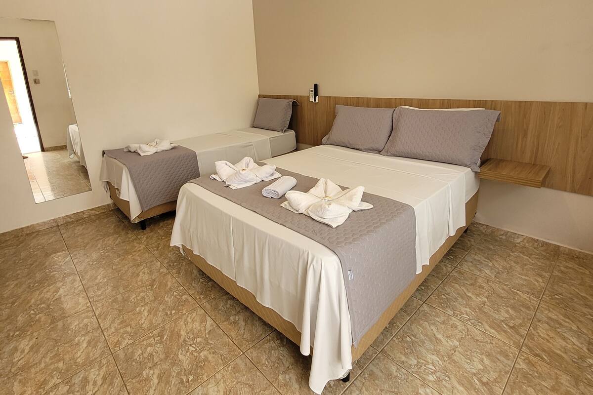 Une chambre d’hôtel avec deux lits, une tête de lit en bois, un climatiseur blanc et un sol carrelé.