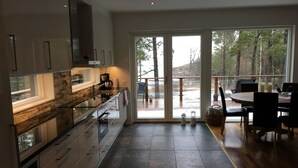 A modern kitchen with a stone backsplash, a dining area with a round table and chairs, and a view of a snowy deck and trees through large sliding glass doors. - Seaside villa in the Nordic Archipelago (Geta)