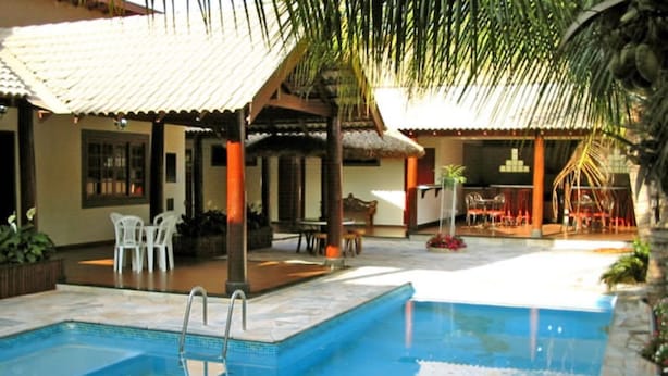 Una piscina con borde de baldosas, rodeada de mobiliario exterior y palmeras.