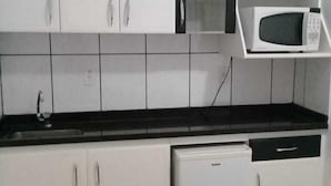 Una cocina compacta con armarios blancos, encimera negra, microondas y un refrigerador pequeño.