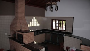 Una cocina con horno de ladrillo, un lavamanos y un ventanal con persianas.