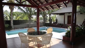 Un espacio al aire libre cubierto con piscina, sillas de mimbre blanco y suelo de baldosas.