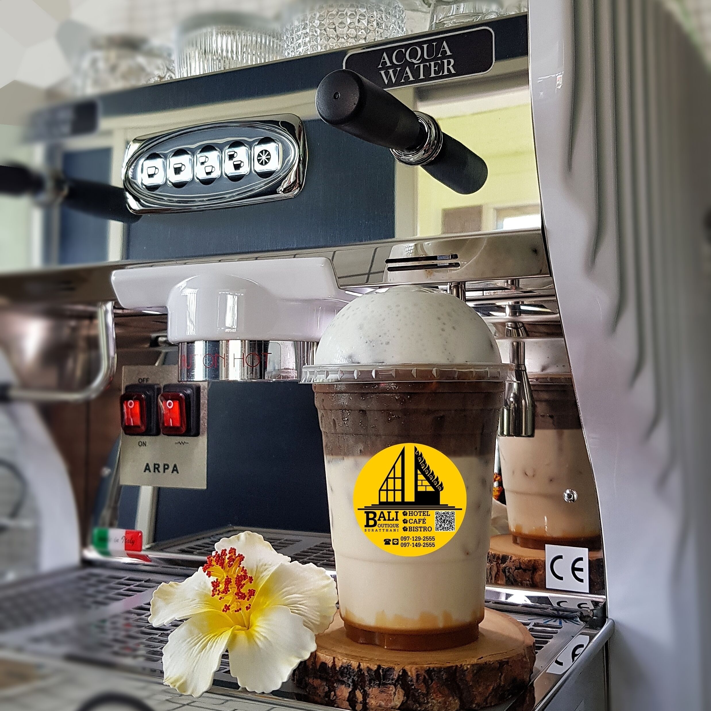 Una cafetera con depósito de agua y una taza de café helado con un logo.
