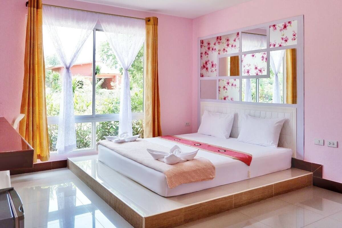 A bedroom with a bed, a window with curtains, a bedside table, and a mirror.