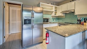 A modern kitchen with a stainless steel refrigerator, a built-in microwave, and a granite countertop. - Walk to Turtle Beach from Kailua-Kona Apt! (Kailua-Kona)