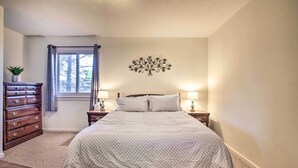 A bedroom with a bed, nightstands, a dresser, a window with curtains, and a wall decoration. - Ski-In Ski-Out Wintergreen Condo w/ Balcony (Wintergreen Resort)