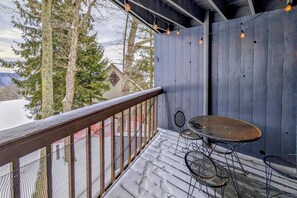 Une terrasse en bois avec une rambarde en métal, deux chaises en métal et une table.