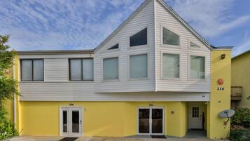 A two-story building with a yellow facade and white trim, featuring two ground-level entrances and a small balcony on the upper floor.