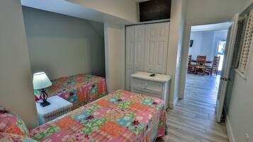 A bedroom with two beds, a nightstand with a lamp, a dresser, and a closet.