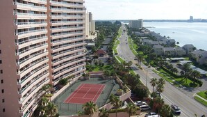 Un hotel de gran altura con múltiples balcones, una cancha de tenis y vista al frente marítimo.