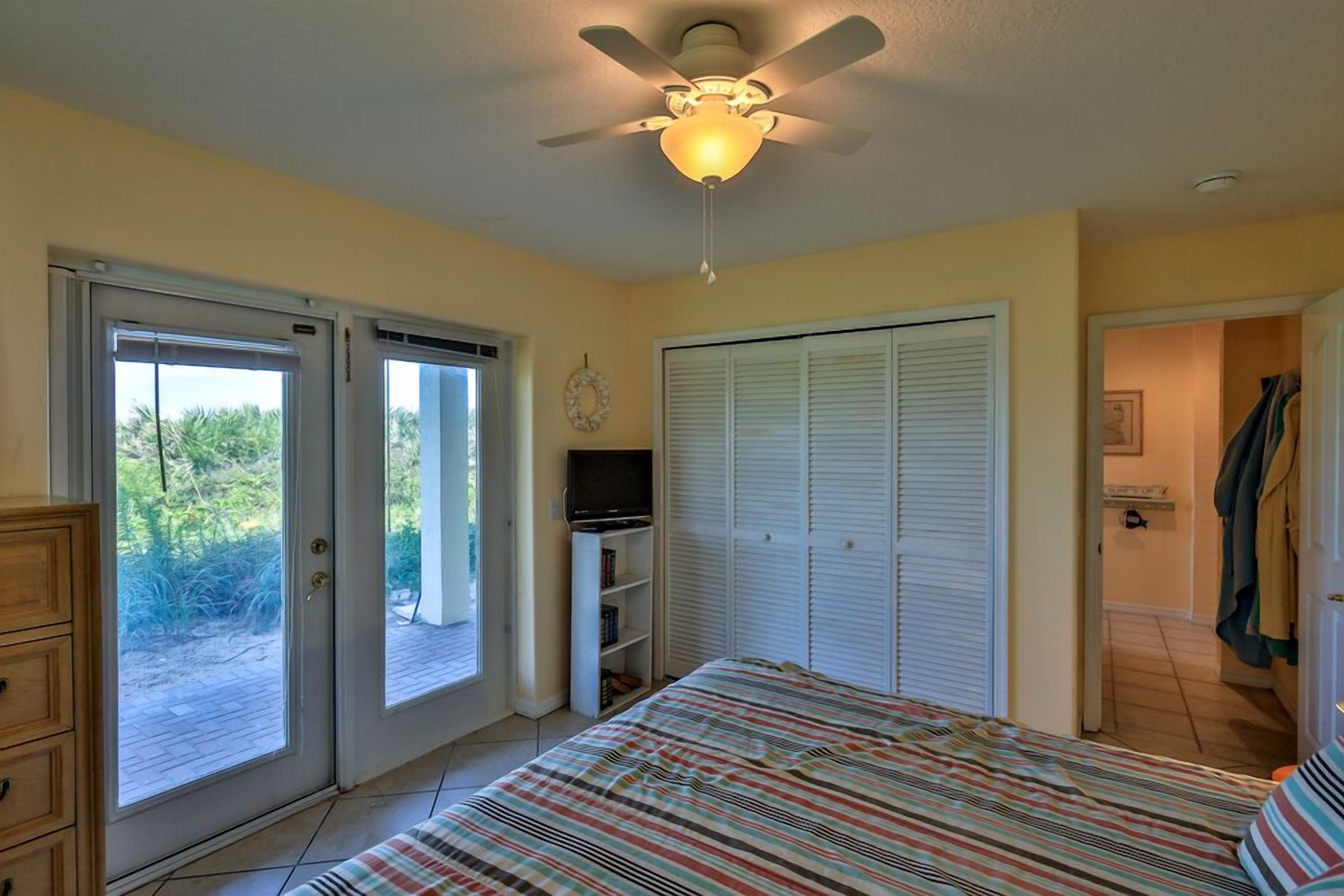 A bedroom with a bed, a ceiling fan, a TV, and a sliding glass door leading to a balcony.