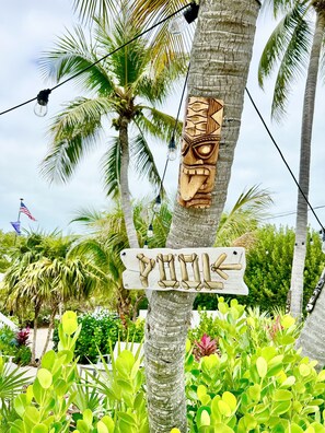 Un letrero de madera con la palabra "PIILA" y una decoración de máscara tiki en un árbol.