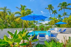 Un área de piscina con sombrillas azules, sillas de descanso blancas y palmeras.