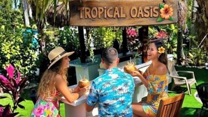 A tropical oasis with a wooden sign, lush greenery, and a table with people. - TikiBar with TV &Stereo, PrivateSpa, Heated Pool, Hammock,SUP’s, Kayaks,Bikes,FP (Islamorada)