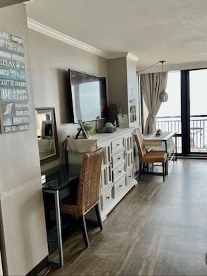 Amplia sala de estar con un televisor de pantalla plana grande, una mesa de comedor con sillas, un mueble blanco y un balcón con vistas.
