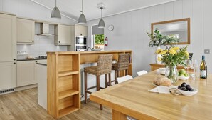 A modern kitchen with wooden cabinetry, a central island with bar stools, a dining table with a vase of flowers, and a wine bottle. - The Retreat, Strawberryfield Park -  a lodge that sleeps 4 guests  in 2 bedrooms (Cheddar)
