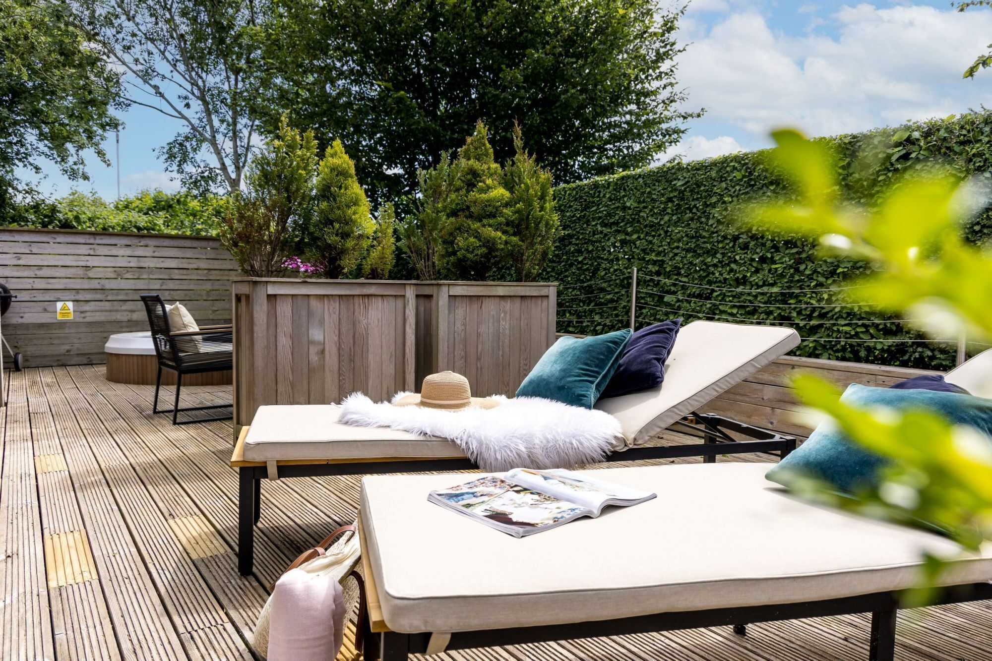 An outdoor deck with two lounge chairs, a wooden table, and a small seating area.