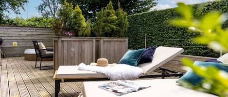 An outdoor deck with two lounge chairs, a wooden table, and a small seating area.