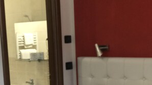 A hotel room with a white bed, a red accent wall, and a visible bathroom with a sink and mirror. - An oasis of peace among secular olive trees (San Pietro Infine)