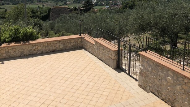 A terrace with stone walls and a tiled floor, overlooking a valley with greenery and distant mountains. - An oasis of peace among secular olive trees (San Pietro Infine)