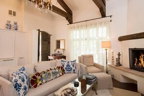 Uma sala de estar com sofá, poltrona, lareira e lustre.