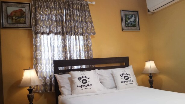 Une chambre d’hôtel avec un lit, deux lampes de chevet, une fenêtre avec des rideaux à motifs et deux tableaux encadrés accrochés aux murs.