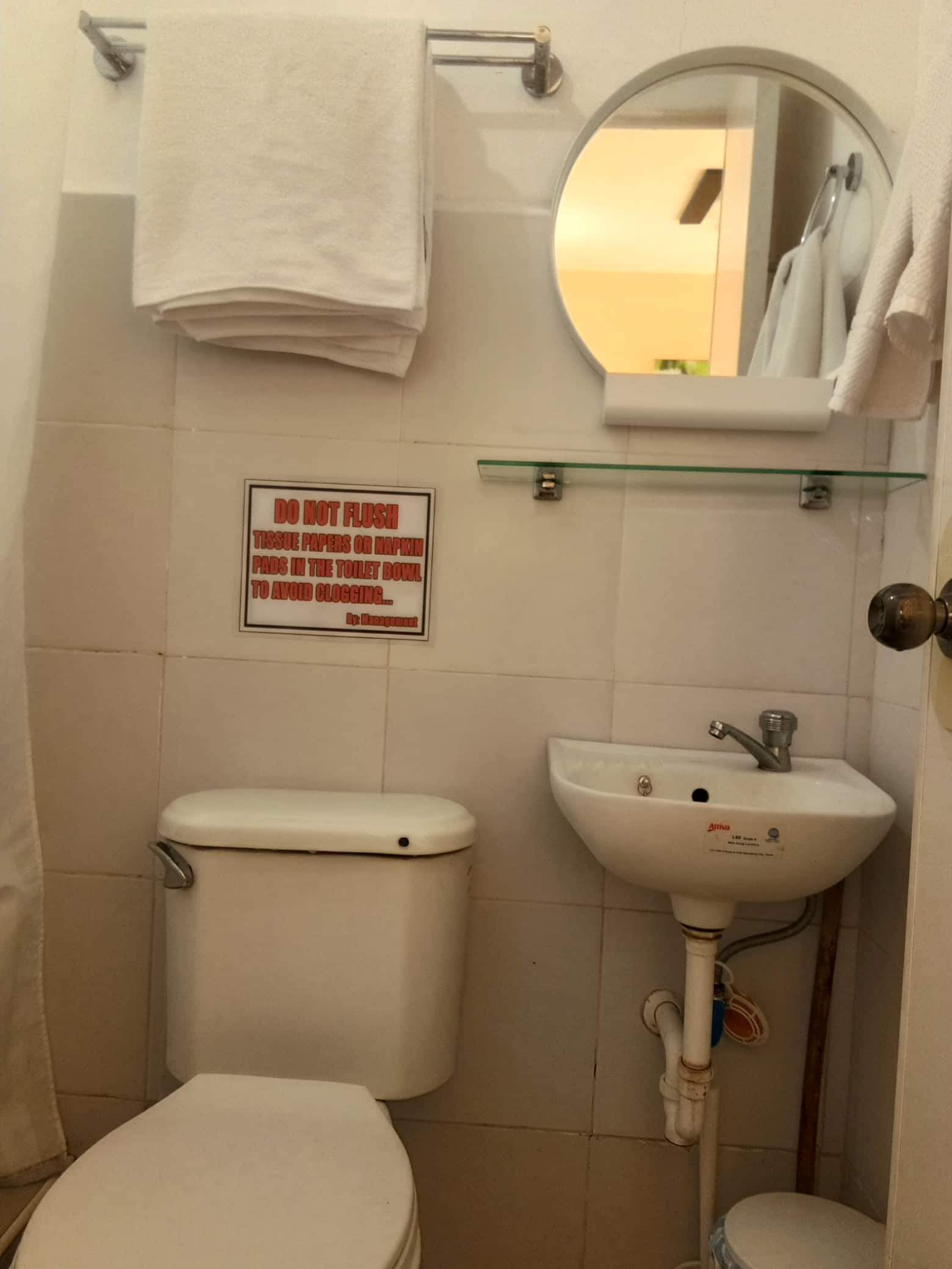 A bathroom with a toilet, sink, and a sign advising not to flush tissue papers or napkins in the toilet bowl to avoid clogging.