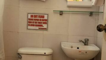 A bathroom with a toilet, sink, and a sign advising not to flush tissue papers or napkins in the toilet bowl to avoid clogging.