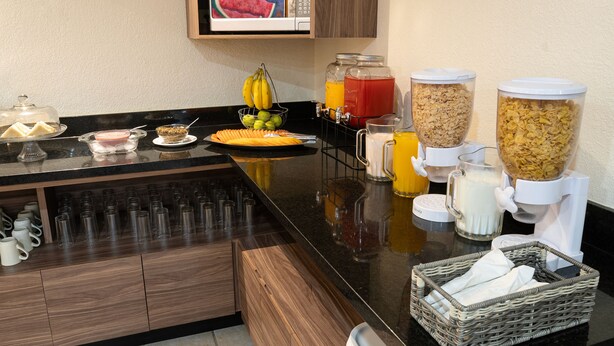 A breakfast bar with various food items and beverages, including a fruit bowl, cereal, and juice dispensers.