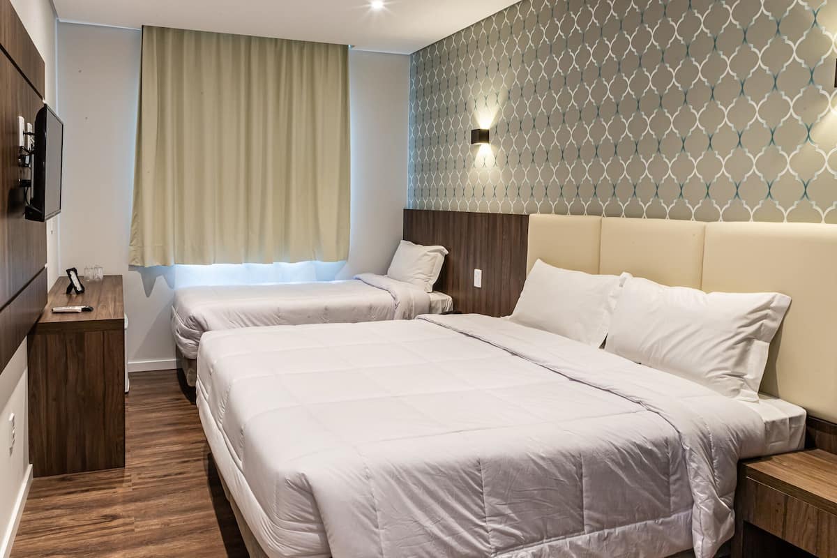 Una habitación de hotel con dos camas, televisión, mesita de noche de madera y pared con diseño.