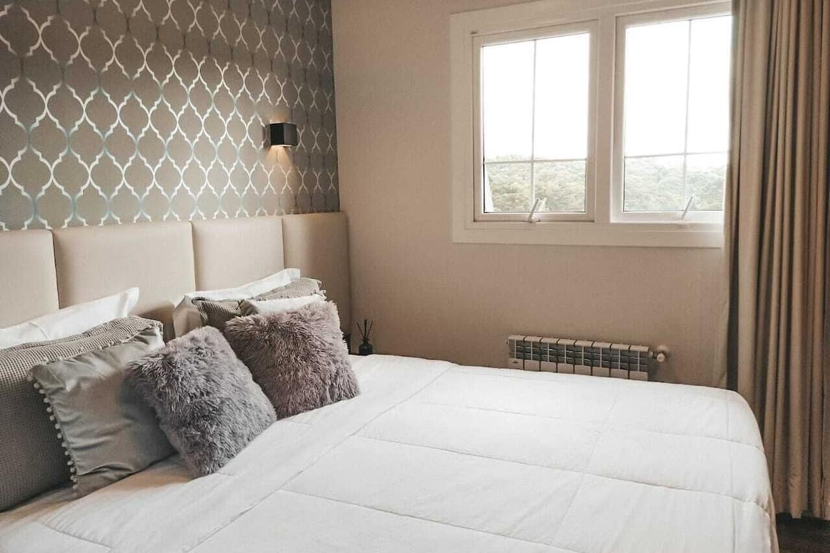 Un dormitorio con una cama grande, un cabecero con diseño geométrico, una ventana con cortinas y un radiador.