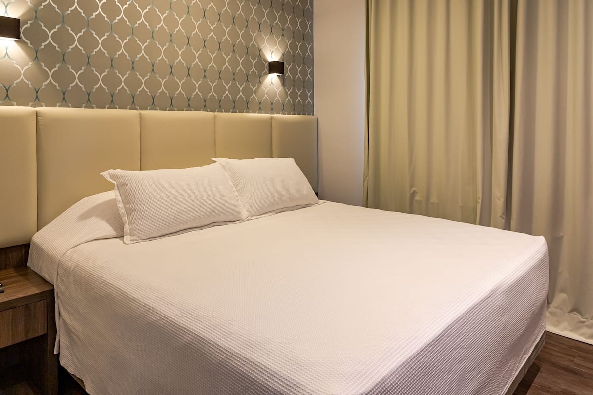 Una cama bien hecha con cabecera, una mesita de noche y una pared con diseño geométrico.