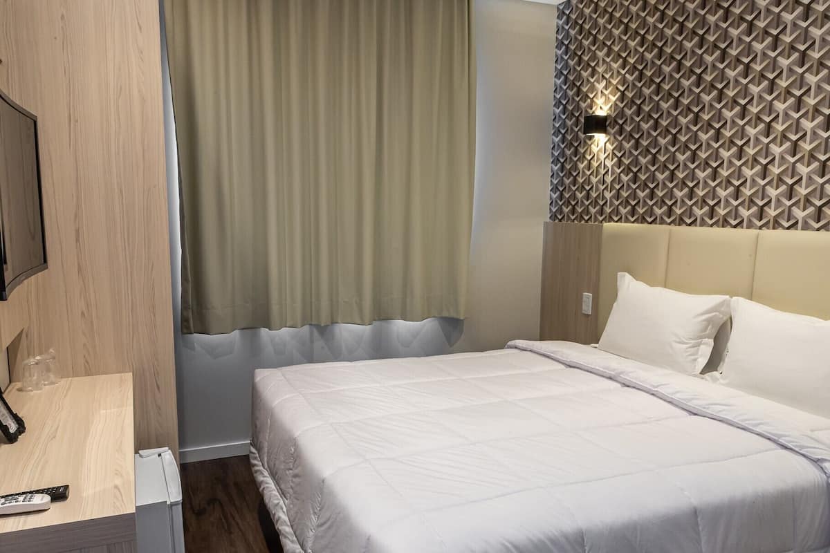 Una habitación de hotel con una cama, un televisor y una lámpara fijada a la pared.