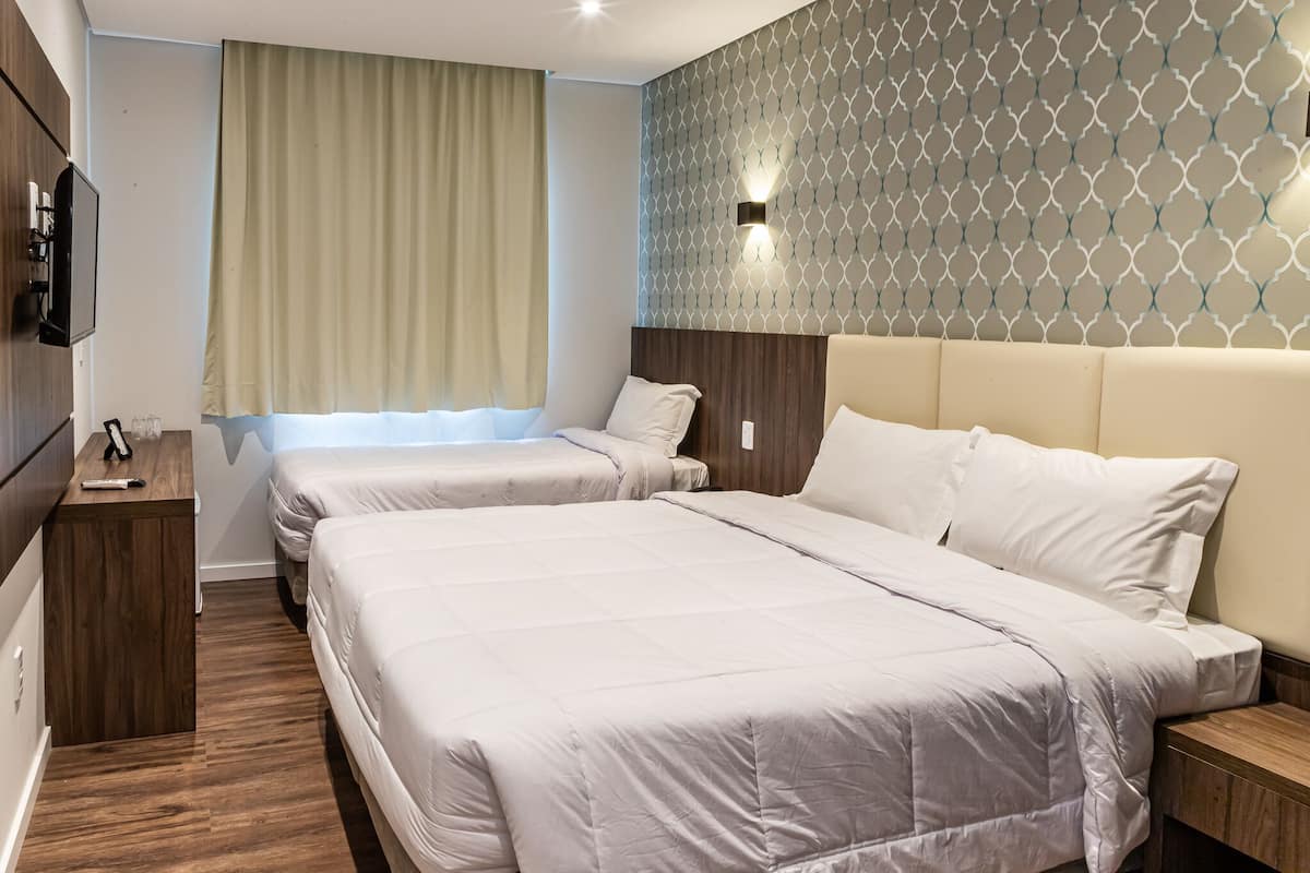Una habitación de hotel con dos camas, televisión, una mesita de noche de madera y pared con diseño.