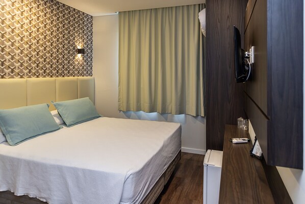 A hotel room with a bed, a TV mounted on the wall, a wooden cabinet, and a window with curtains.