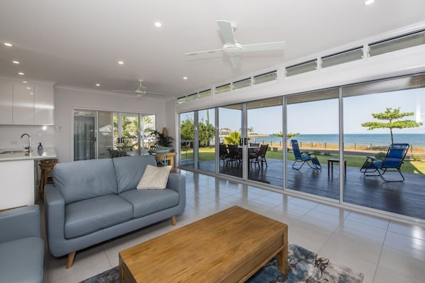 Ein modernes Wohnzimmer mit Sofa, Couchtisch und großen Fenstern mit Blick auf eine Terrasse und das Meer.