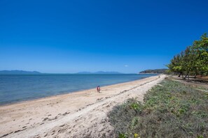 Ein Strand mit blauem Himmel, sandigem Ufer und einer Person, die spazieren geht.