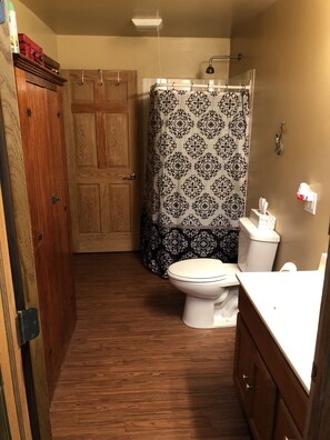 Un baño con puerta de madera, cortina de ducha con estampado en blanco y negro, inodoro y lavamanos con espejo.