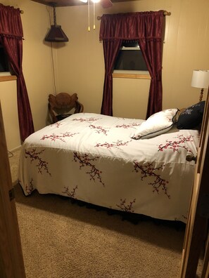 Un dormitorio con cama, una silla, una ventana con cortinas y una lámpara colgante.
