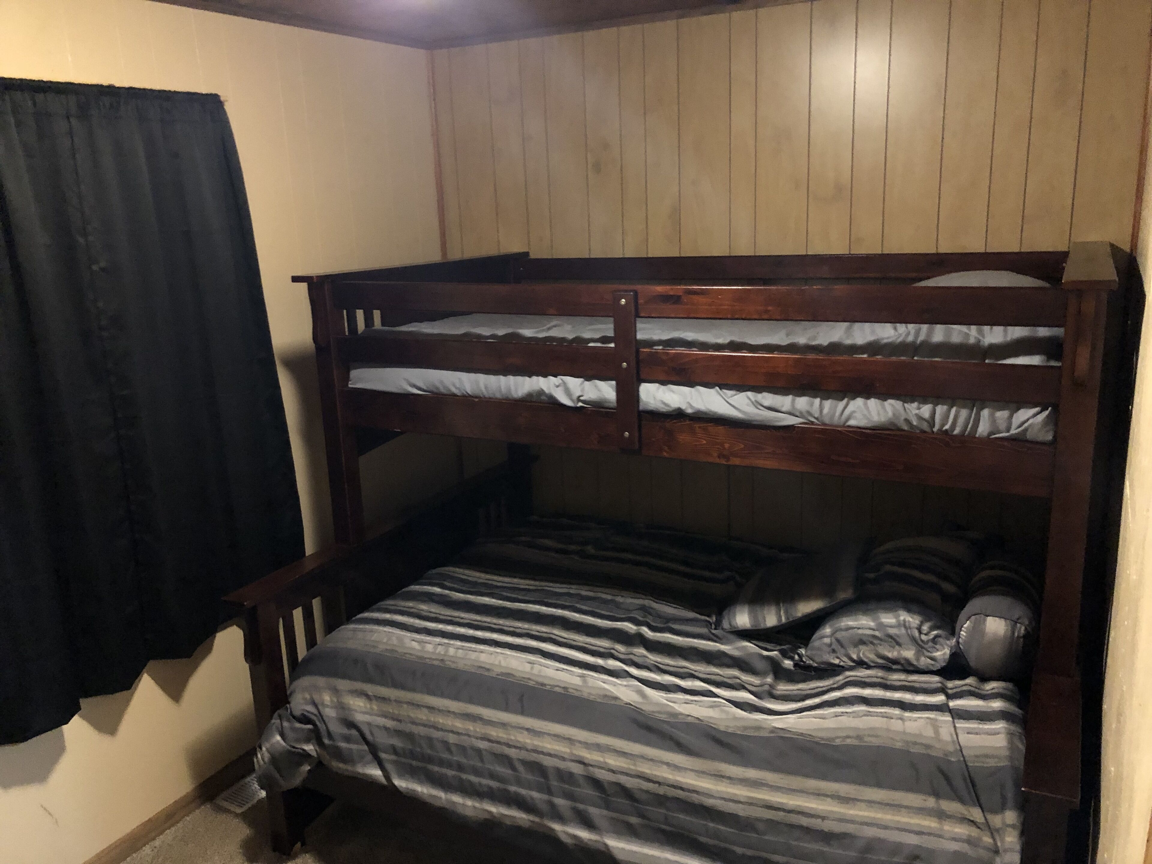 A bunk bed with striped bedding in a room with wooden walls and a black curtain.