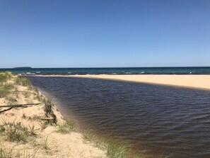 Una playa con un canal de agua estrecho, dunas arenosas y un cielo despejado.
